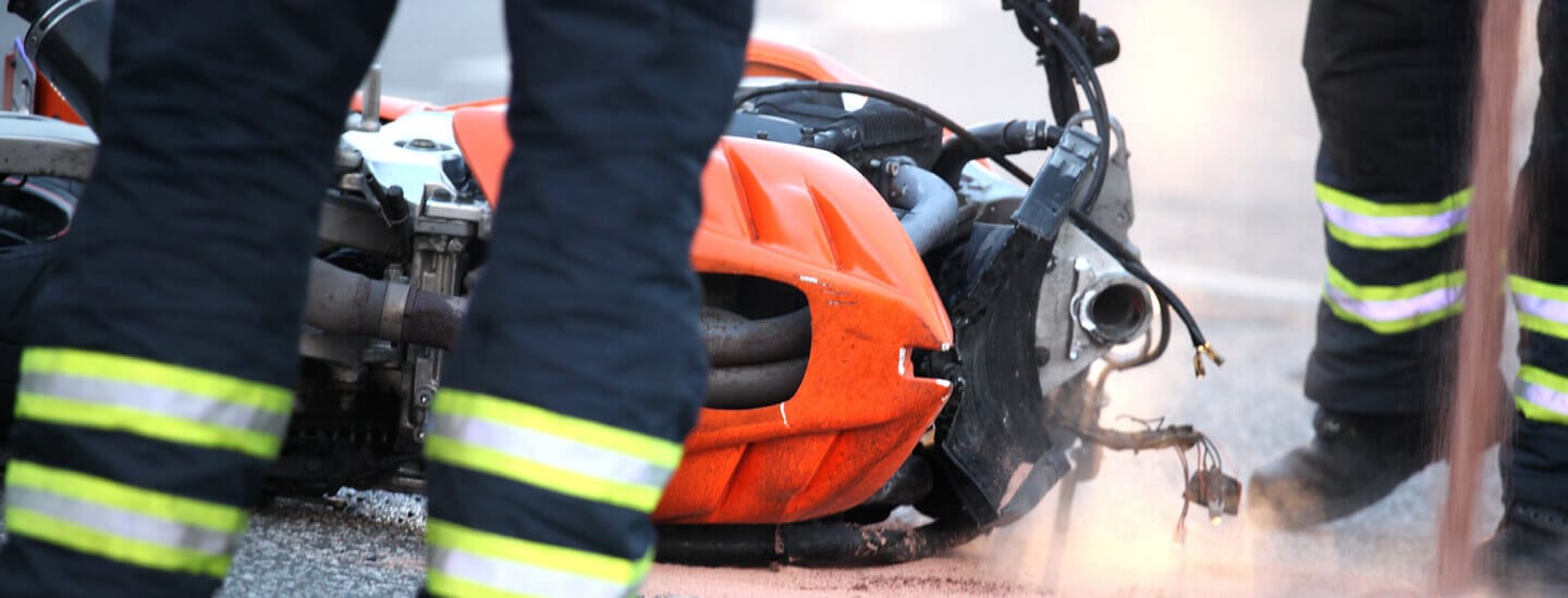 Close up image of a motorcycle on it's side in the road after what appears to be an accident as you see legs of firefighters