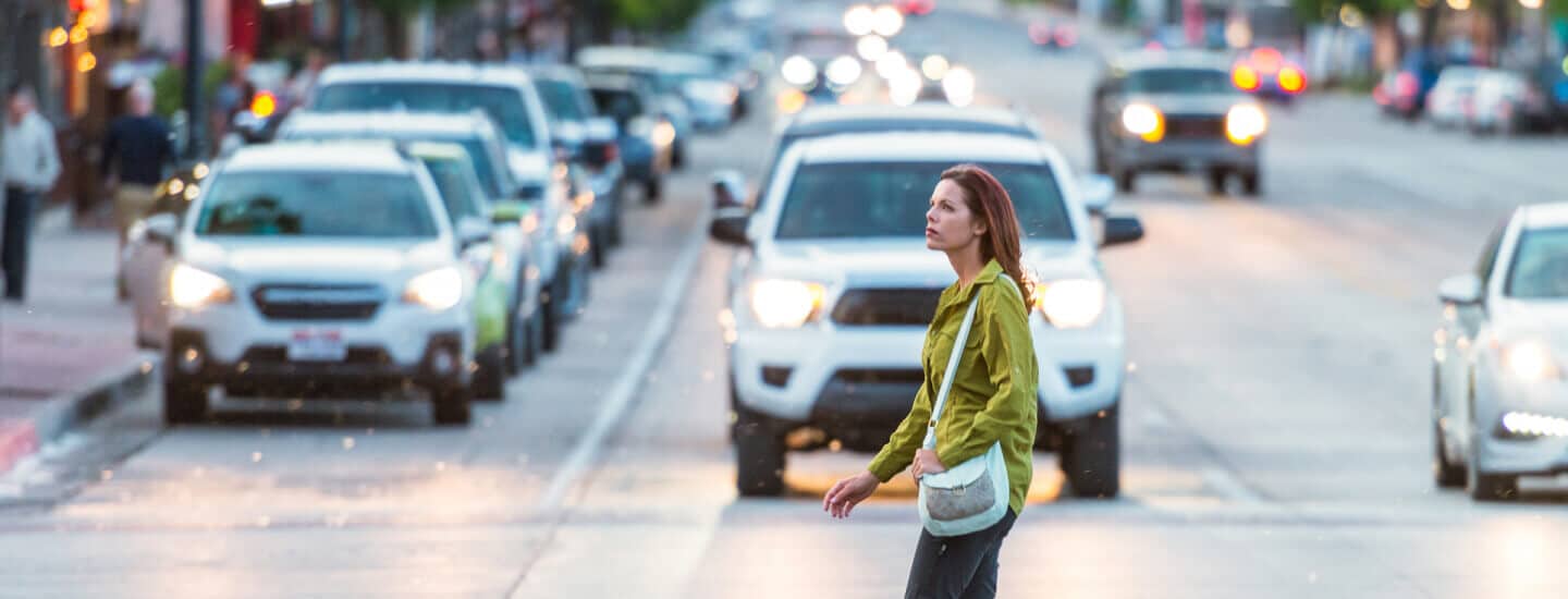 A woman crossing the street with a lot of cars behind her.