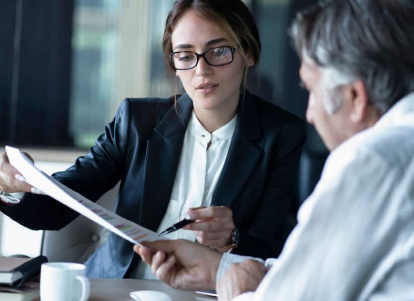 A woman in glasses showing a man paperwork.